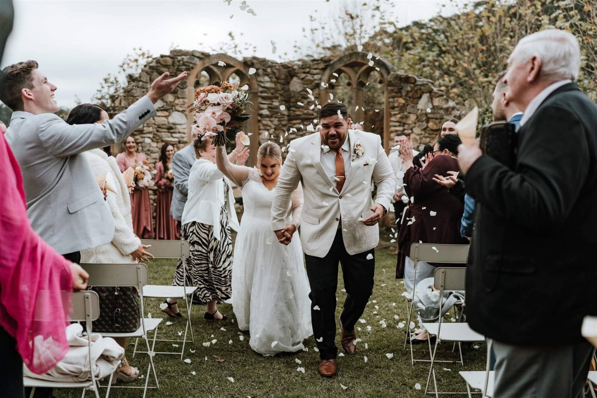 joyful bride and groom walking down the aisle as guests throw petals