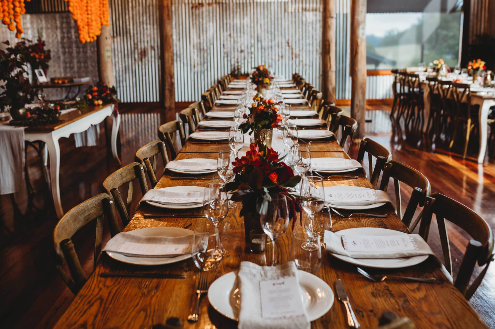 Rustic wedding reception setting with a long wooden table, vintage chairs, and autumnal floral centerpieces