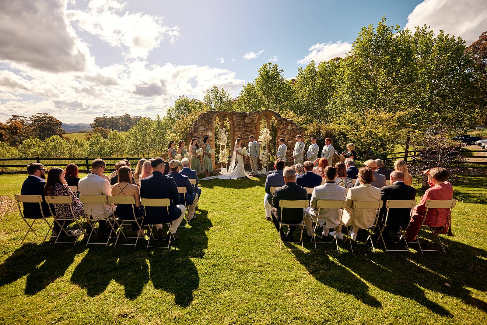 Wedding guests seated for an outdoor ceremony with a scenic view, facing the bride, groom, and wedding party at the ruins mali brae farm