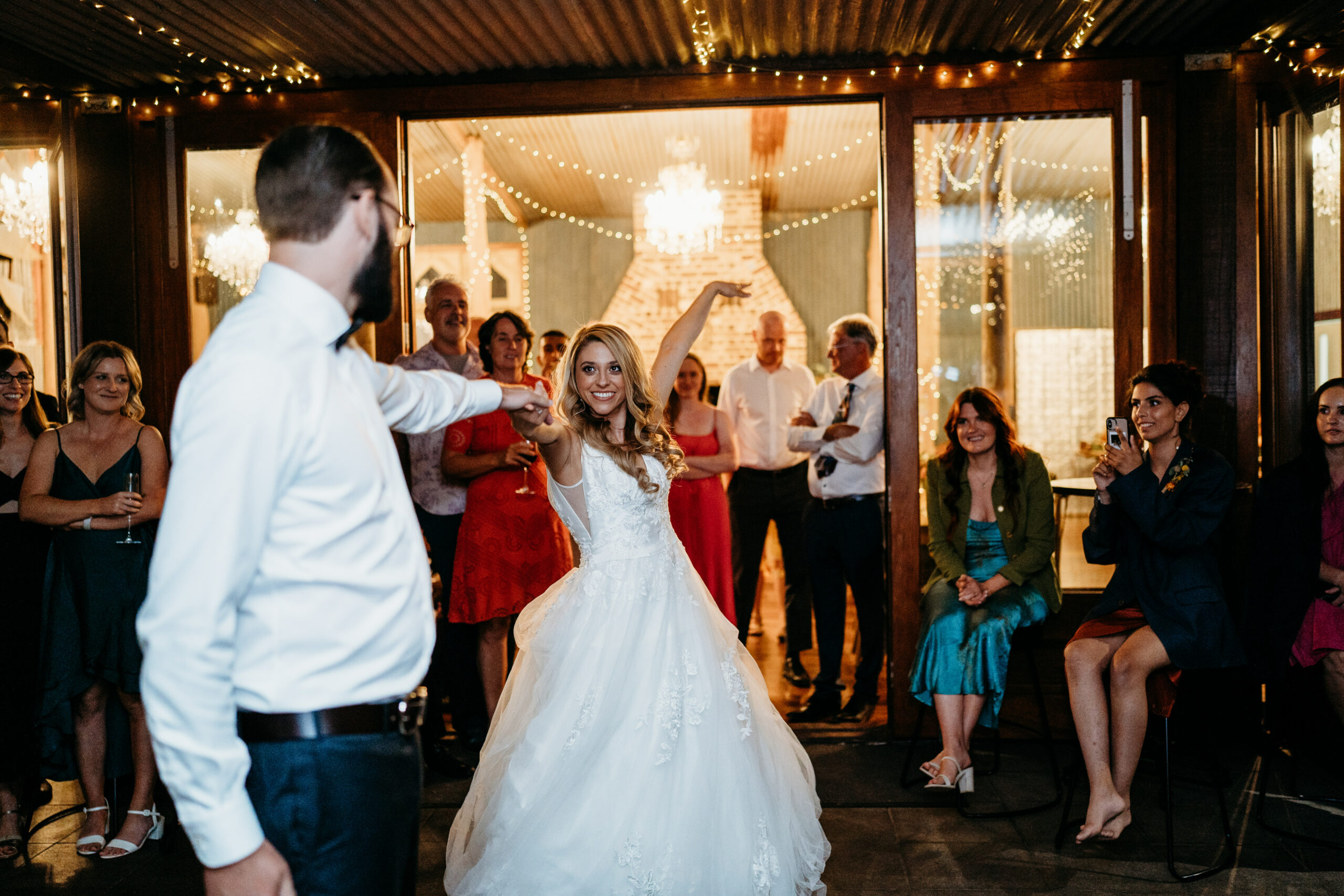 First dance of the bride and groom in a warmly lit reception hall, with guests surrounding them